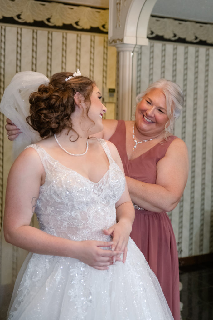 kentucky wedding photographer klem photography captures bride as she looks back at mother in bridal suite after getting her long flowy veil placed 