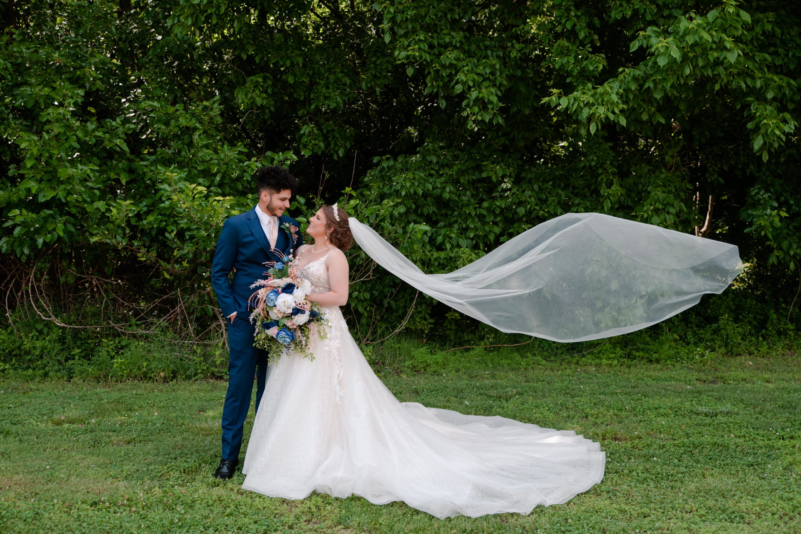 bride with flowy veil looks at her groom in blue tux by kentucky wedding photographer klem photography