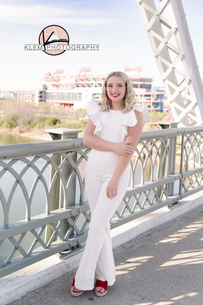 senior pictures in kentucky with senior girl standing on a bridge with the city skyline behind her
