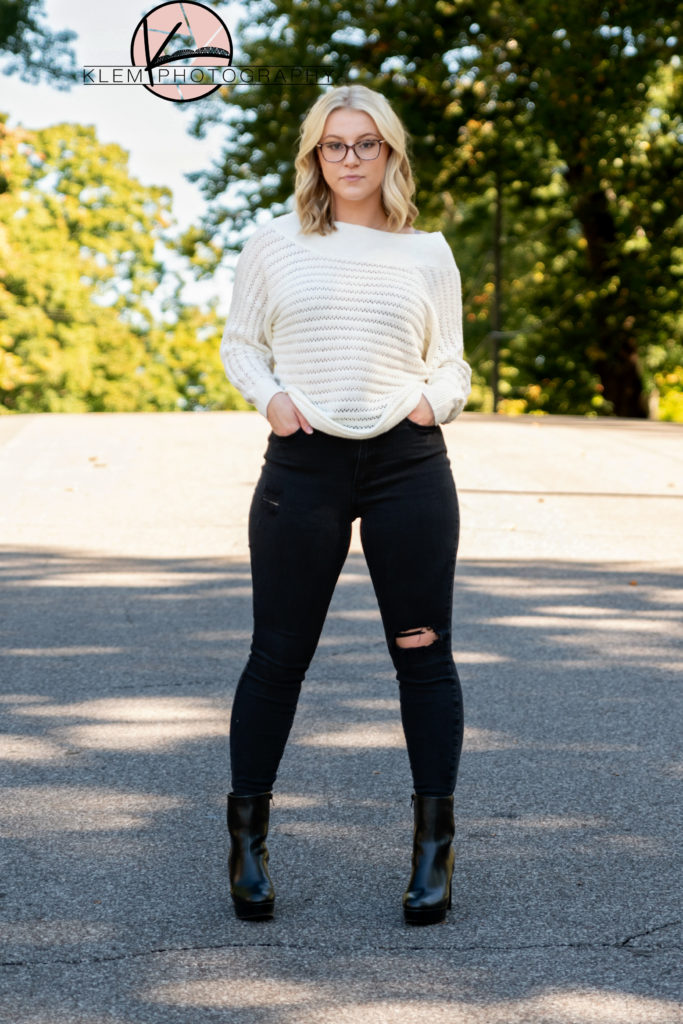 kentucky fall senior pictures with senior girl wearing a neutral sweater, black distressed jeans, and black booties as she stands in the middle of main street henderson ky doing a straight model pose 