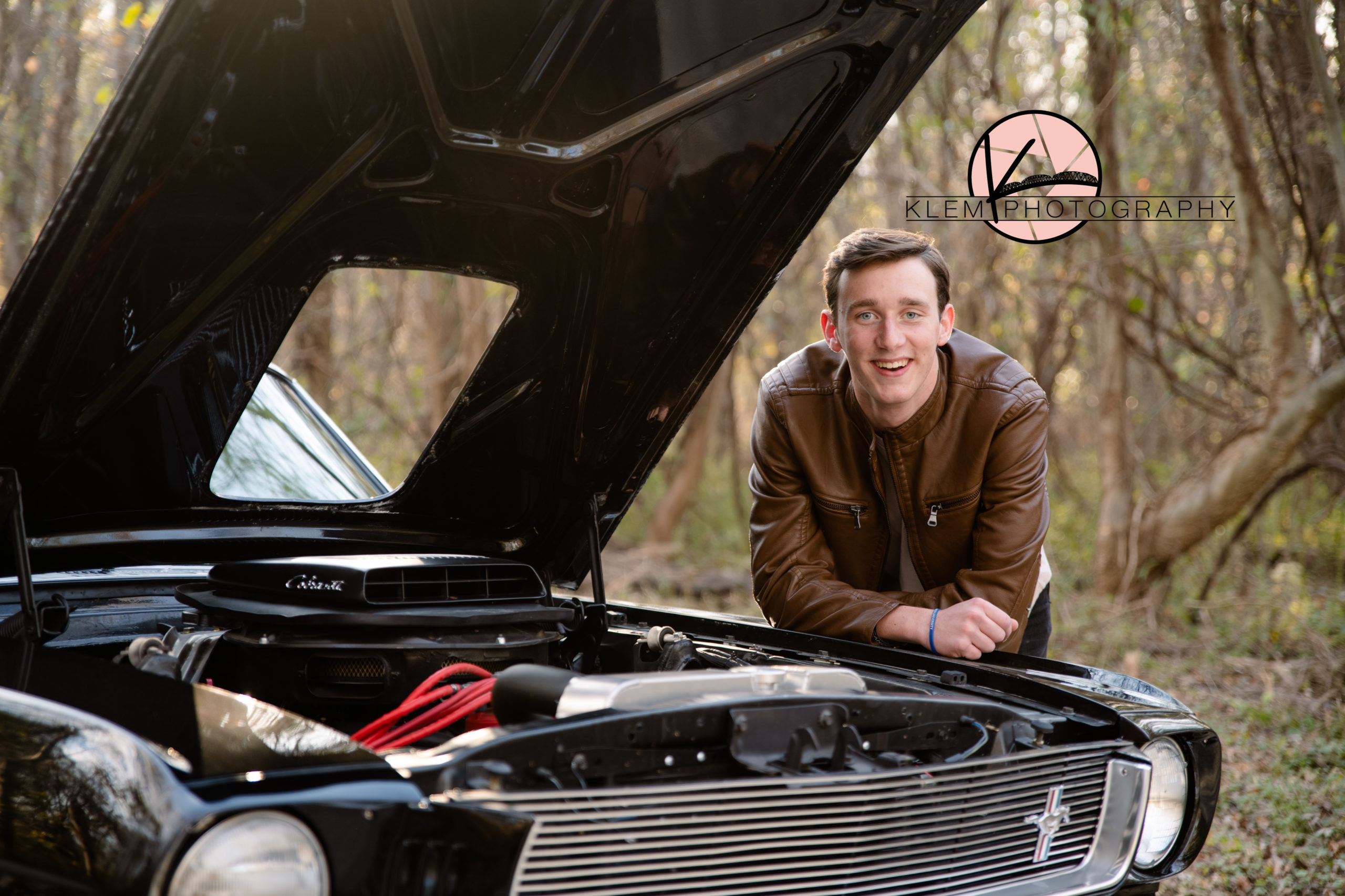 Senior Pictures Evansville IN senior guy stands looking over the engine of his classic black mustang