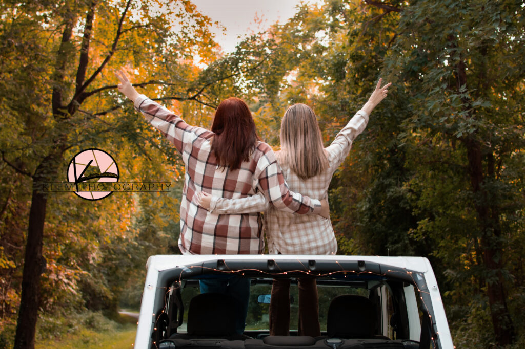 fall senior portraits in henderson ky by klem photography. 2 high school senior girls sit on the top of a white jeep with their backs facing the camera as they both hold out a peace sign