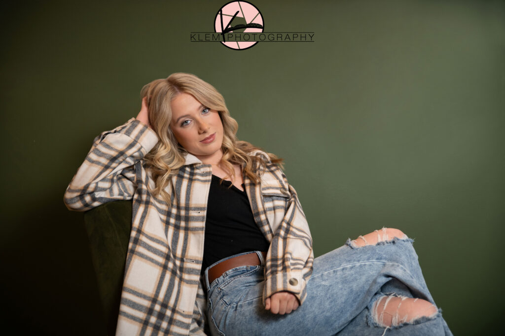 fall senior pictures at coffee shop with girl sitting in chair in front of green wall wearing a plaid button up and black tank top by klem photography henderson ky senior pictures