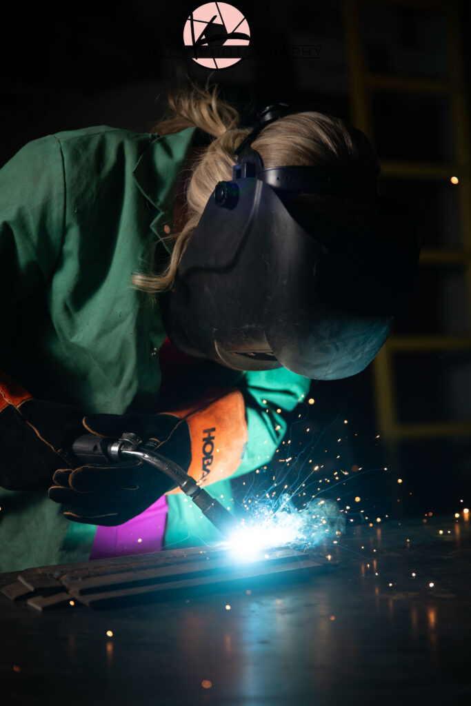 senior girl wearing a welding helmet as she welds an arc weld for her senior pictures in henderon ky by klem photography