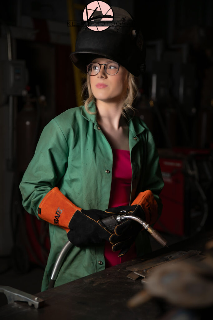 welding senior pictures with girl in hot pink jumpsuit wearing welding helmet looking off to the side as she holds a cutting torch in her hands by klem photography henderson ky senior photographer
