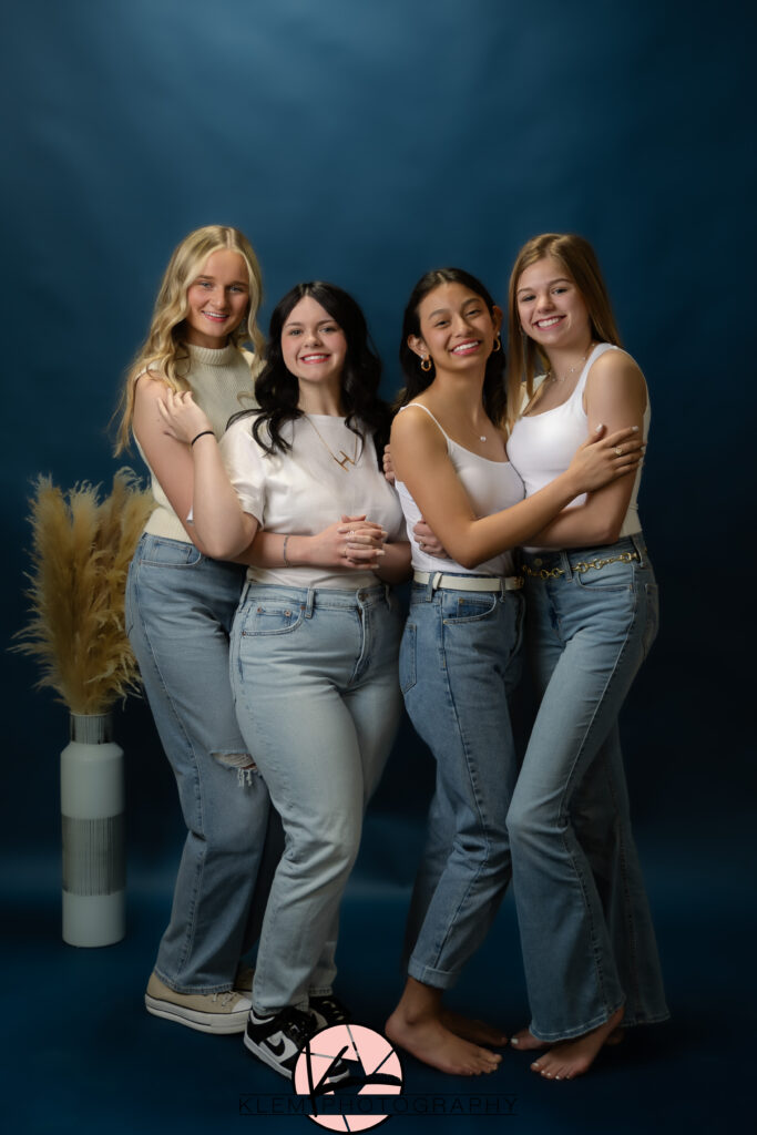 klem photography model team girls wearing white shirts with denim blue jeans with a solid navy backdrop taking the best senior pictures near me with their best friends all hugging