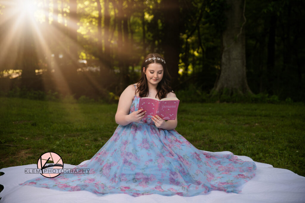 Evansville best senior photographers with klem photography at Audubon Park in Henderson KY as girl sits in blue prom dress reading Persuasion by Jane Austin.