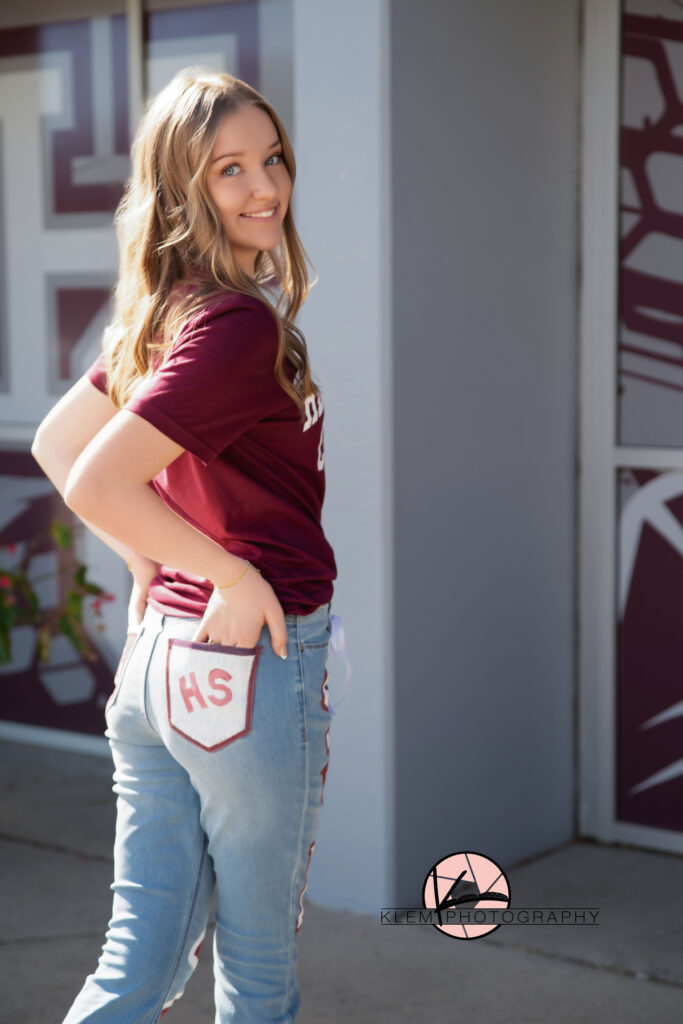 Henderson KY senior pics with klem photography and girl standing in front of henderson county high school with hands in back pockets and smiling at camera