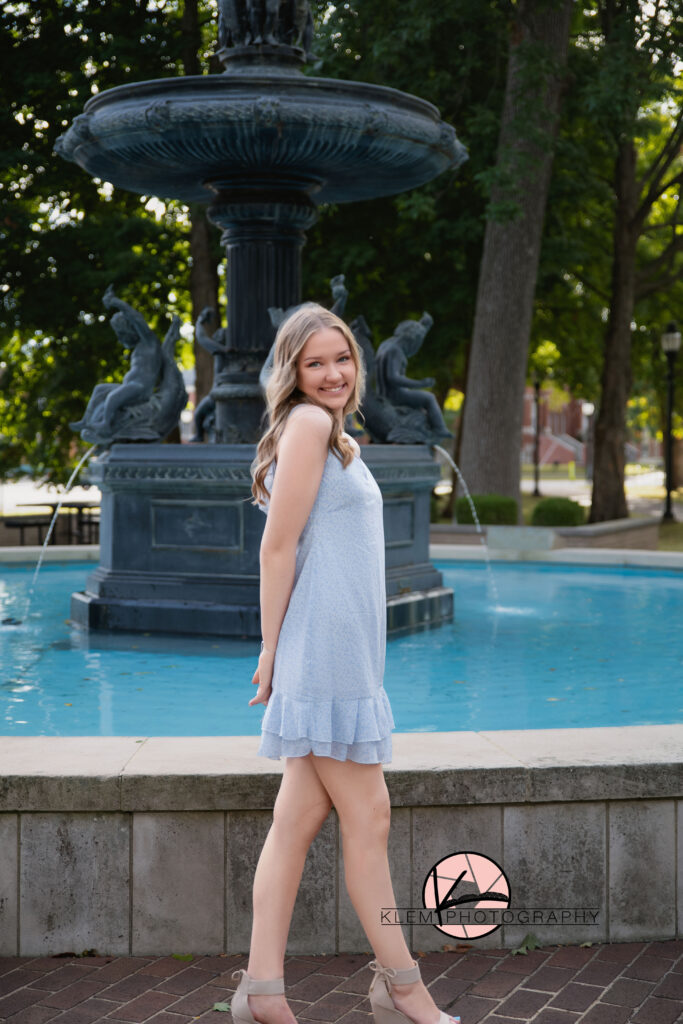 Henderson KY senior pics with Klem Photography senior girl wearing blue dress standing in front of water fountain at central park 